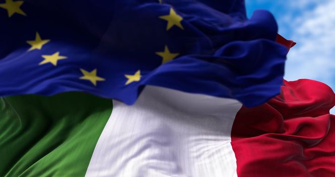 The national flag of Italy waving in the wind together with the European Union flag blurred in the foreground. Politics and finance. Italy is a member state of the European Union