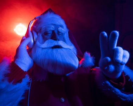 Santa claus listens to music with headphones at a party. Blue red neon light and smoke