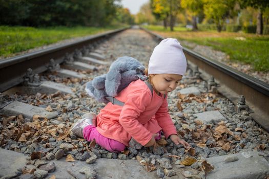 little girl sitting on the railroad tracks. toddler plays on railroad in forest