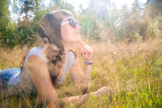 beautiful young woman in sunglasses enjoys the sun on the grass in warm sunshine