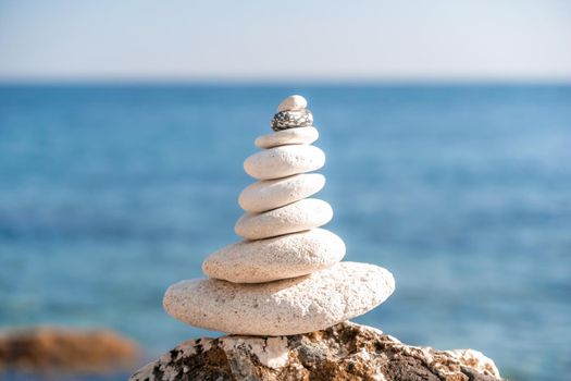 Balanced pebbles pyramid on the beach on sunny day and clear sky at sunset. Golden sea bokeh on background. Selective focus, zen stones on sea beach, meditation, spa, harmony, calm, balance concept.