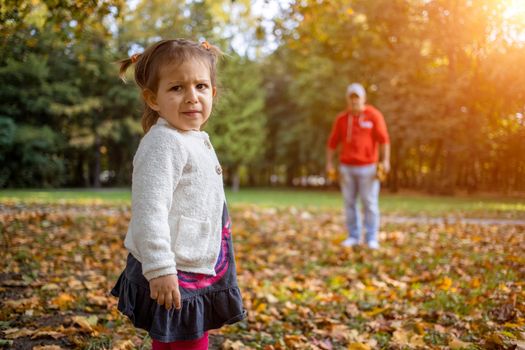 disgruntled child in the park with dad. angry girl in the park looks at the camera. father and daughter Toddler walk in the autumn park