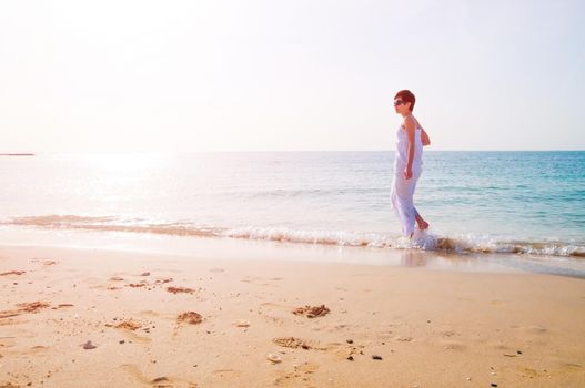 Young brunette woman in summer white dress standing on beach and relaxing at sunset