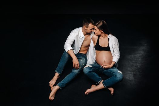 a pregnant woman and a man in a white shirt and jeans in a studio on a black background.