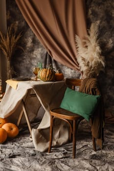 Autumn interior: a table covered with dishes, pumpkins, chair, casual arrangement of Japanese pampas grass. Interior in the photo Studio.