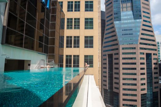 young caucasian woman relaxing in a pool on the roof of a skyscraper in a metropolis under the sun....