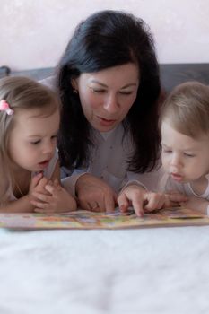 Grandmother with grandson and granddaughter in bed reading a book. Grandmother with grandchildren in bed during distance learning. Grandma plays with her grandchildren in bed during quarantine