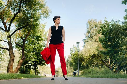 Portrait of a girl in a red suit standing in the alley of the park.