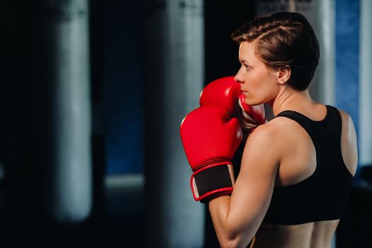 portrait of a female boxer in red gloves in the gym during training.