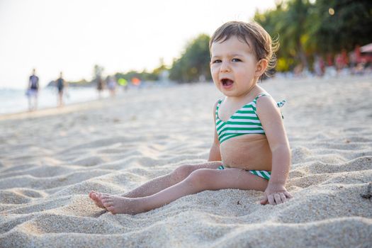 tired toddler girl sitting on sandy bech. little girl yawns on the beach