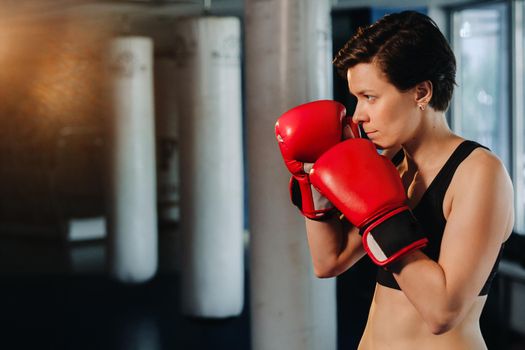 portrait of a female boxer in red gloves in the gym during training.