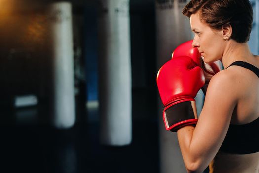 portrait of a female boxer in red gloves in the gym during training.