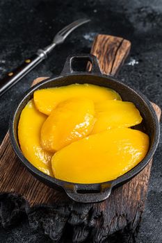 Canned mango slices in bowl. Black background. Top view.