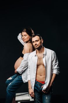 a pregnant woman and a man in a white shirt and jeans in a studio on a black background.