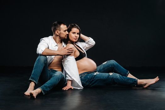 a pregnant woman and a man in a white shirt and jeans in a studio on a black background.