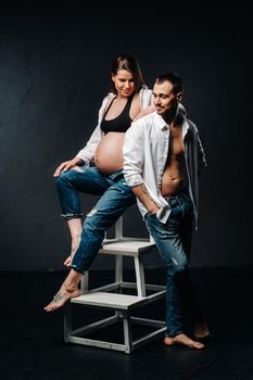 a pregnant woman and a man in a white shirt and jeans in a studio on a black background.