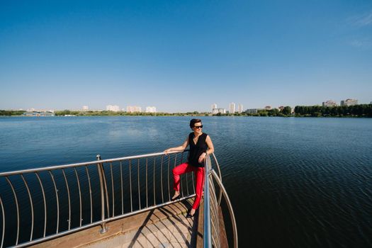 A girl in a red suit stands on a pier near the lake.