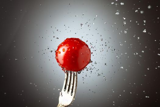 tomato cherry on a fork in splashes of water. Black white background. Copy space