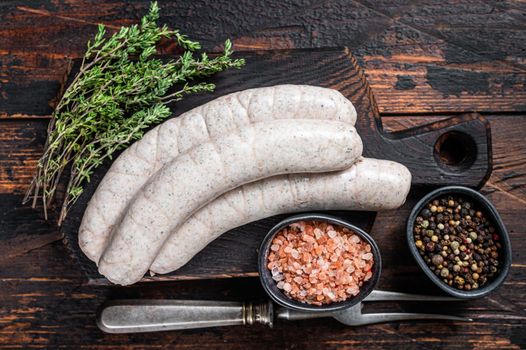Munich traditional white sausages on a wooden board with thyme. Dark wooden background. Top view.
