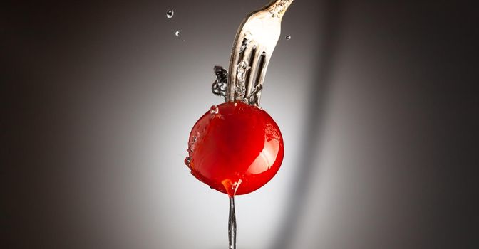 Cherry tomato ripe on a metal fork. A jet of water. Black white gradient background.