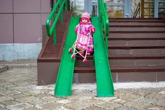 cute toddler drags a toy stroller along the ramp of the stairs. Slope walkway for disabled people, people pushing strollers, carts with stainless bars to prevent falling