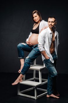 a pregnant woman and a man in a white shirt and jeans in a studio on a black background.