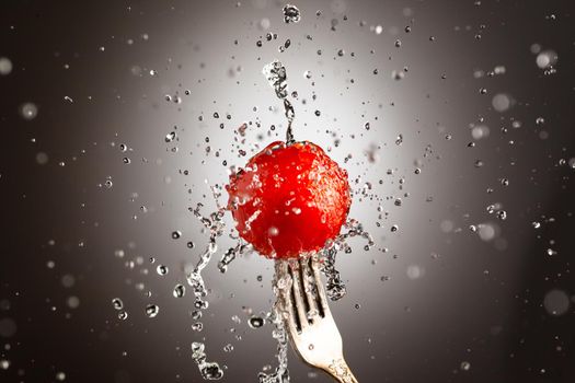tomato cherry on a fork in splashes of water. Black white background. Copy space
