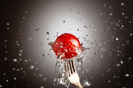 Ripe cherry tomato in splashes of water on a fork.