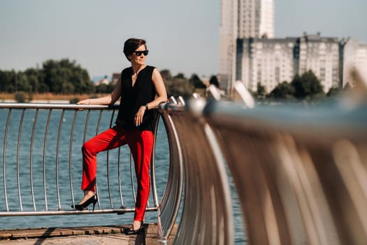 A girl in a red suit stands on a pier near the lake.