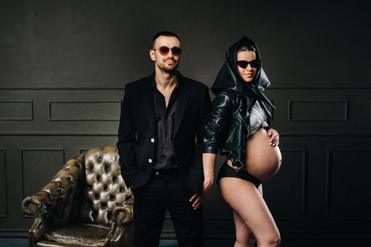 a pregnant woman in black clothes and a headscarf and a man in a suit in a studio on a dark background.