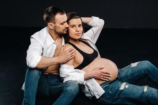 a pregnant woman and a man in a white shirt and jeans in a studio on a black background.