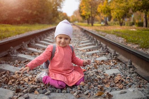 portrait of little girl sitting on the train tracks in the forest