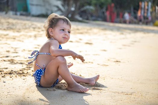 portrait of little cute girl sitting and playing on a beach near the sea on vacations in sunset.