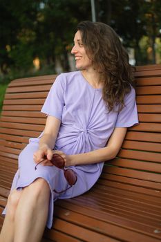 Young girl in light violet dress is having great time during vacation in the summer sitting on the bench, travelling concept.