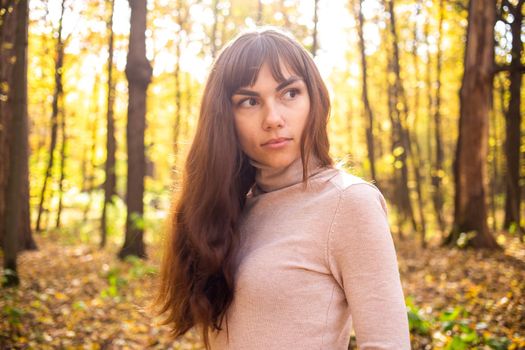 portrait of young beautiful woman in autumn park in sun shines. thinkfull young woman looking away