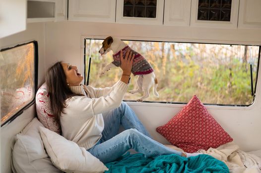 Caucasian woman sitting in a van hugging with dog Jack Russell Terrier. Travel in a camper in the fall