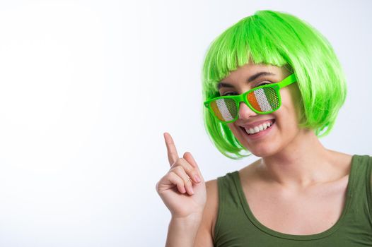 Cheerful young woman in green wig and funny glasses celebrating st patrick's day on a white background.