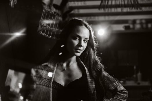 Portrait of a young European girl with long hair in a coffee shop in the evening light, a tall Girl in a jacket with long hair in a cafe. black and white photo.