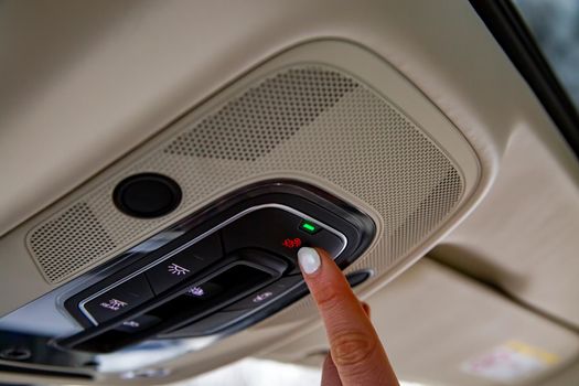 female driver's finger presses sos button on the ceiling panel of a modern car