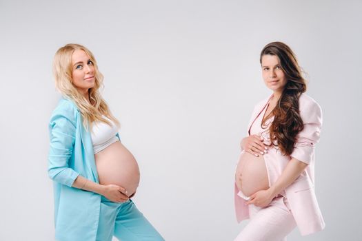 Two pregnant women with big bellies in suits on a gray background.