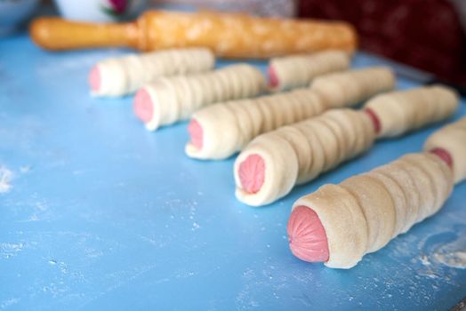 Blanks for fried pies. The sausages are wrapped in thin strips of yeast dough. The dough is rising. Selective focus