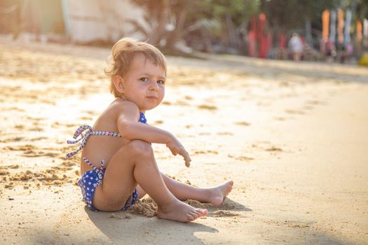 portrait of little girl sitting on a sandy beach in the sun