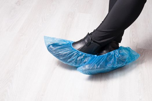 the girl is sitting in black leather boots with shoe covers on them, a light wooden floor, a copy space