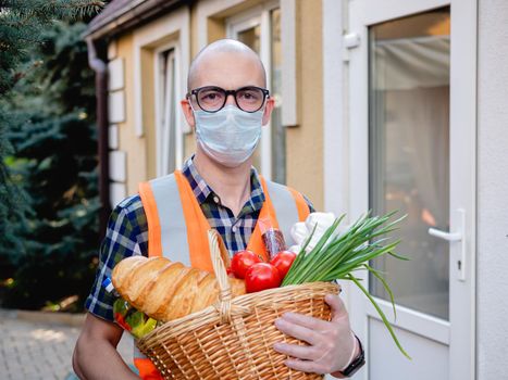 Portrait of a male volunteer in a medical mask near the front door with a basket full of food