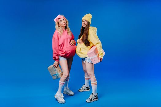 Two pregnant girls with gifts in their hands on a blue isolated background.