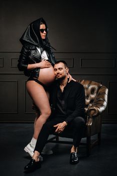 a pregnant woman in black clothes and a headscarf and a man in a suit in a studio on a dark background.