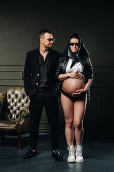 a pregnant woman in black clothes and a headscarf and a man in a suit in a studio on a dark background.