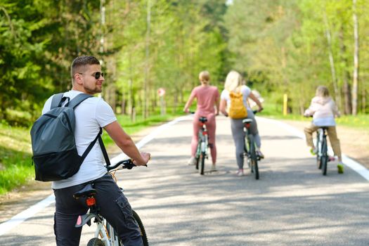 A group of cyclists with backpacks ride bicycles on a forest road enjoying nature.