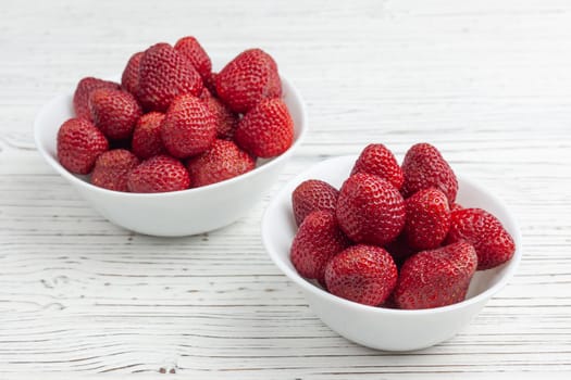 two white plates with strawberries on a white painted wooden background, one standing closer, the other further