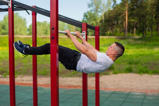 Caucasian man doing a back plank on the uneven bars. Workout on the sports ground